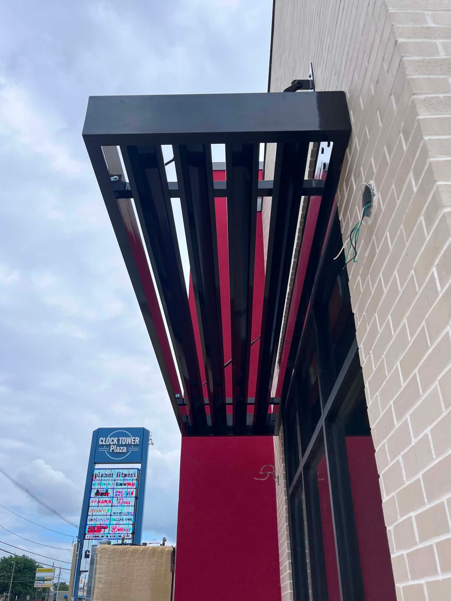 Louvered metal sunshade canopy on red steel supports against a blue sky