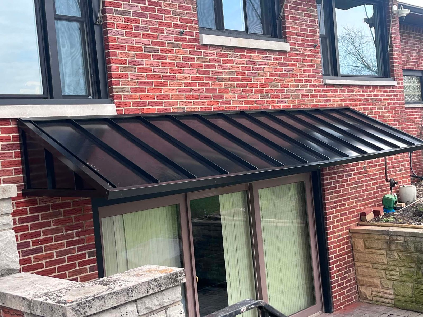 Black standing seam metal awning over a window on a brick home
